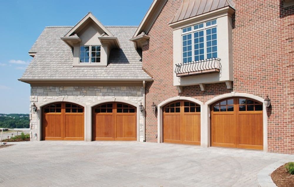 Elegant brick home with wooden garage doors and decorative windows on a sunny day.