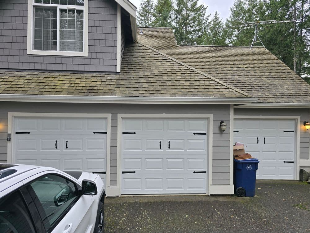 Triple garage with white doors, blue recycling bin, and a car parked in front.