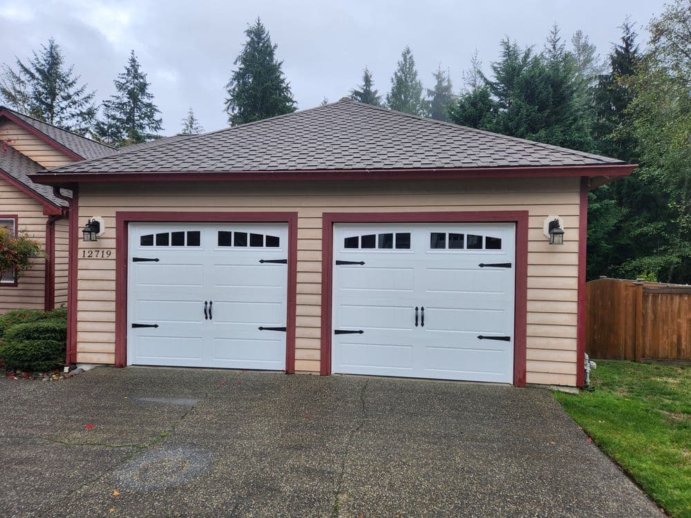 Modern two-car garage with white doors, decorative accents, and landscaped surroundings.