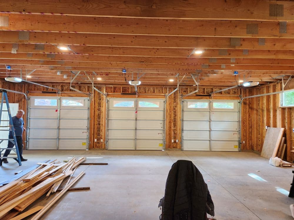 Spacious indoor garage with three garage doors, wooden beams, and construction materials.