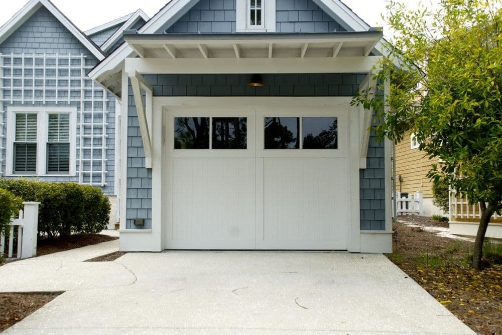 Modern gray house with double garage door and landscaped driveway, surrounded by greenery.