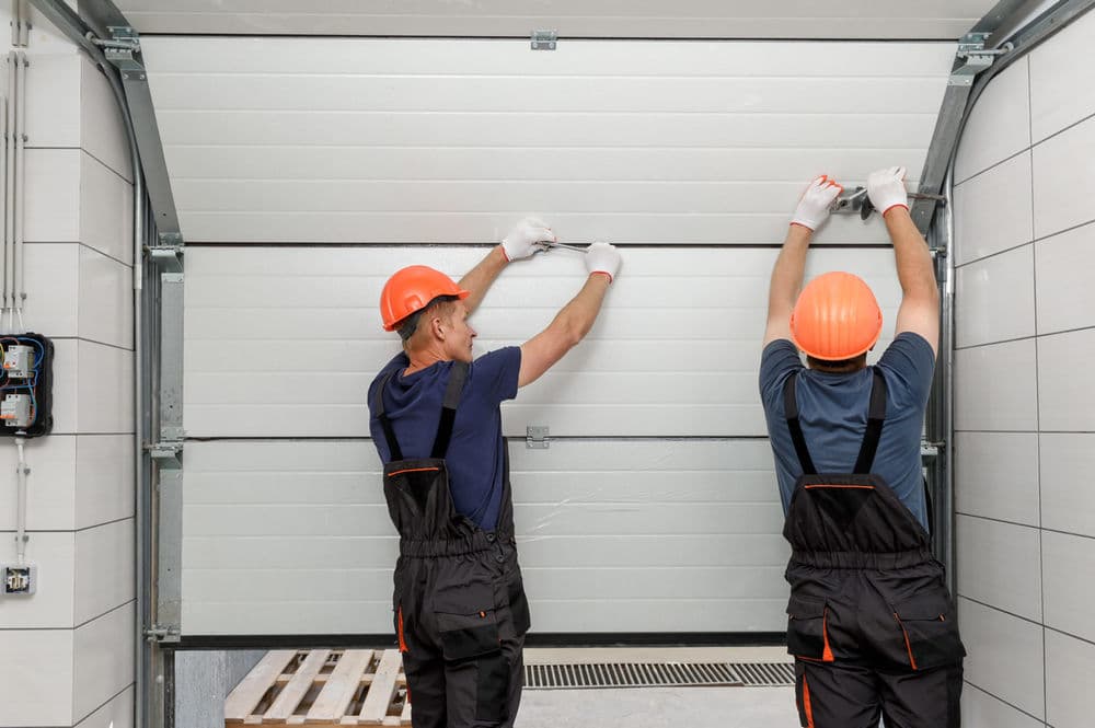 Two construction workers installing a garage door in a modern facility, wearing safety helmets.